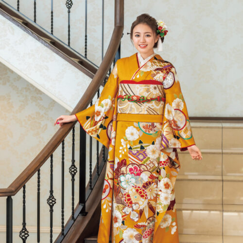 落ち着かせた辛子色の地に、寿ぎを告げる金彩に彩られた糸車が華やか。可憐な桜や椿、万寿菊が溶け合い、誰よりもおしゃれな着姿の完成です。