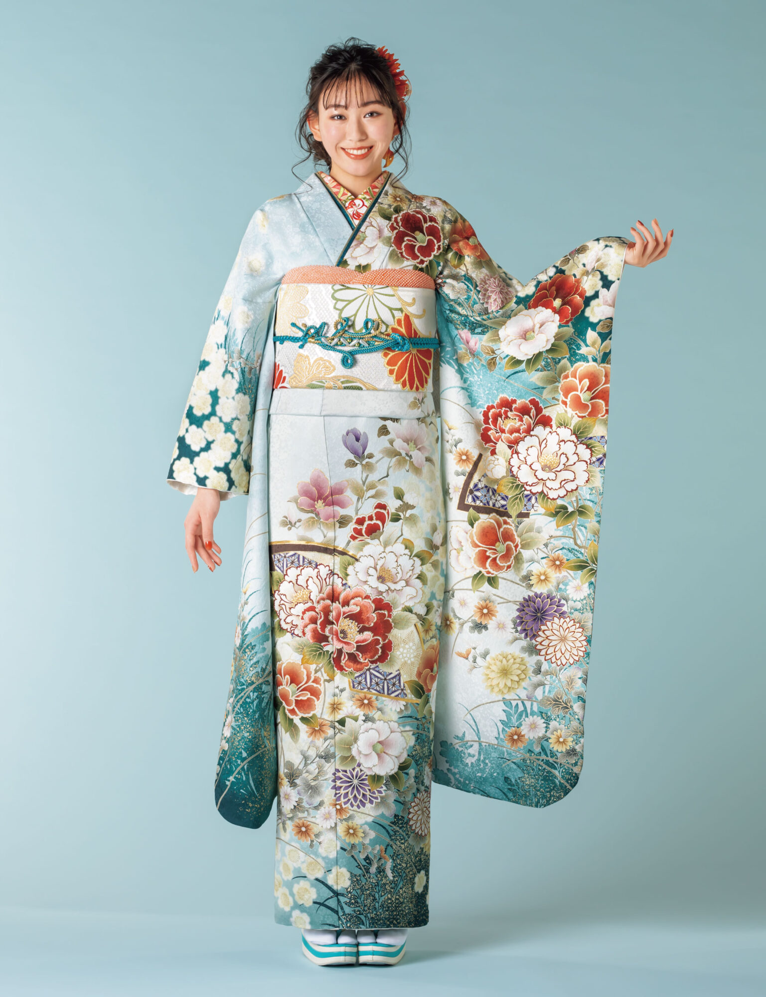 水色から深青への振袖に牡丹や菊をあしらい、金彩と青の帯締を合わせた女性の立ち姿