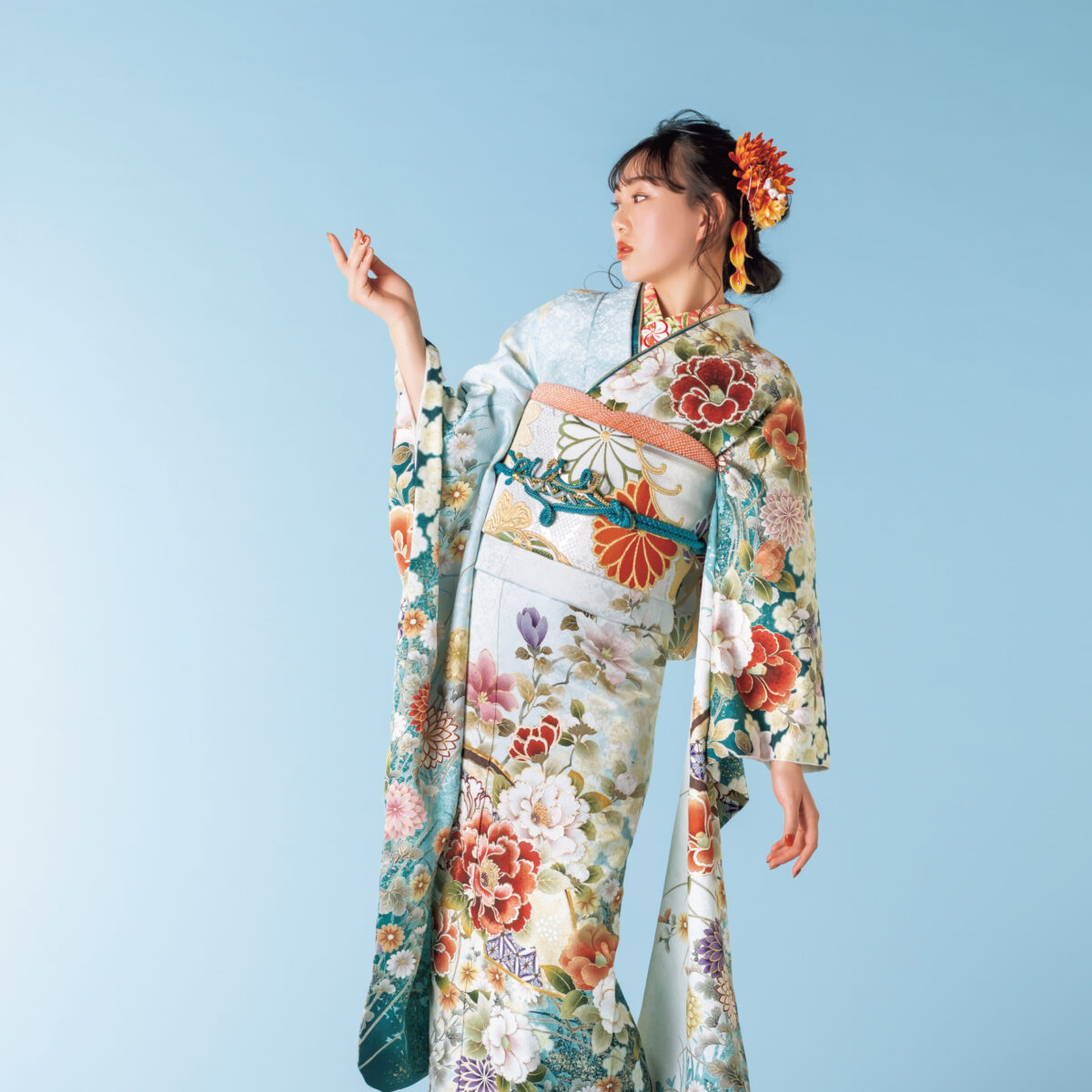 水色から深青への振袖に牡丹や菊をあしらい、金彩と青の帯締を合わせた女性の立ち姿