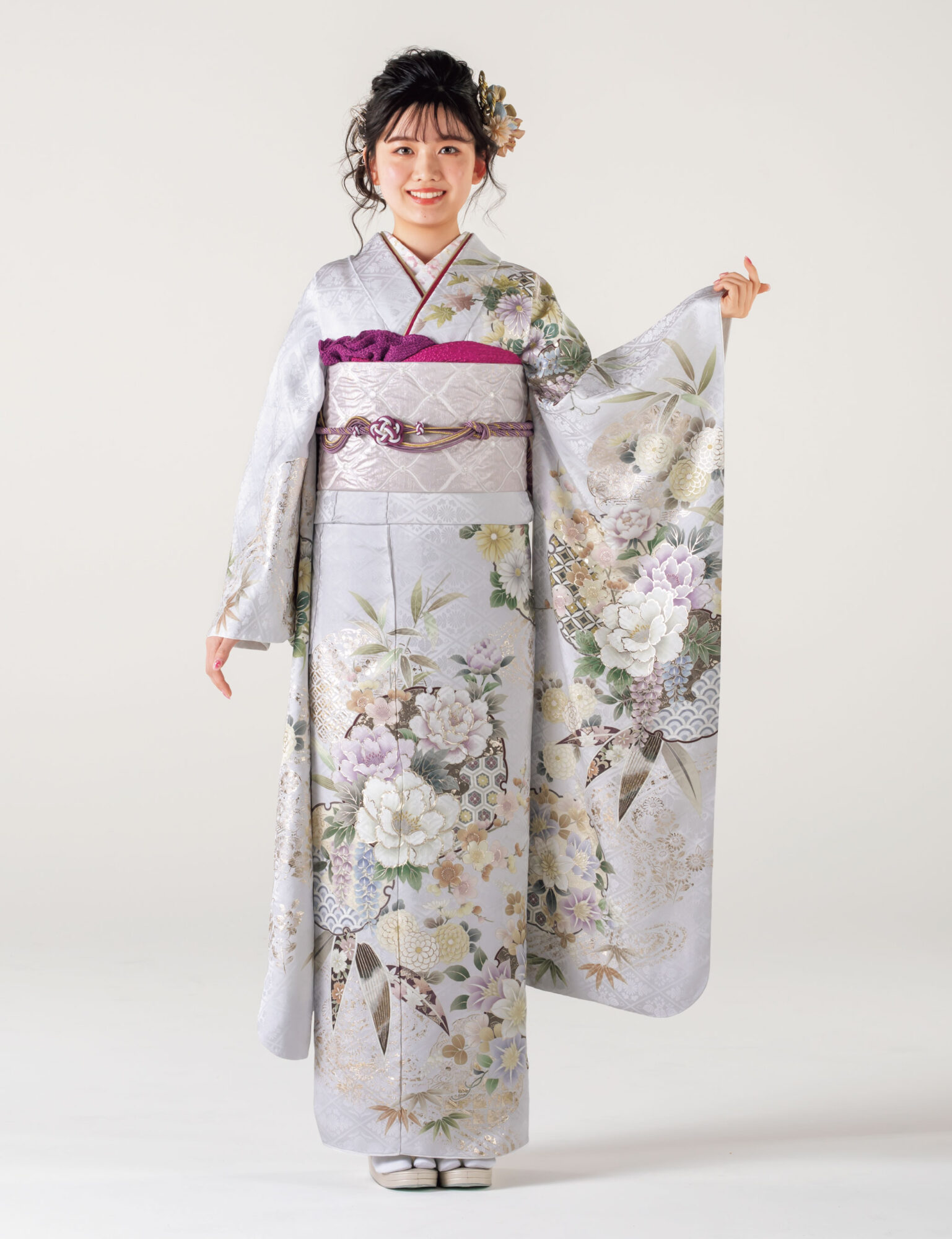 銀鼠色の振袖に白と紫の花々をあしらい、紫の帯締を合わせた女性の立ち姿