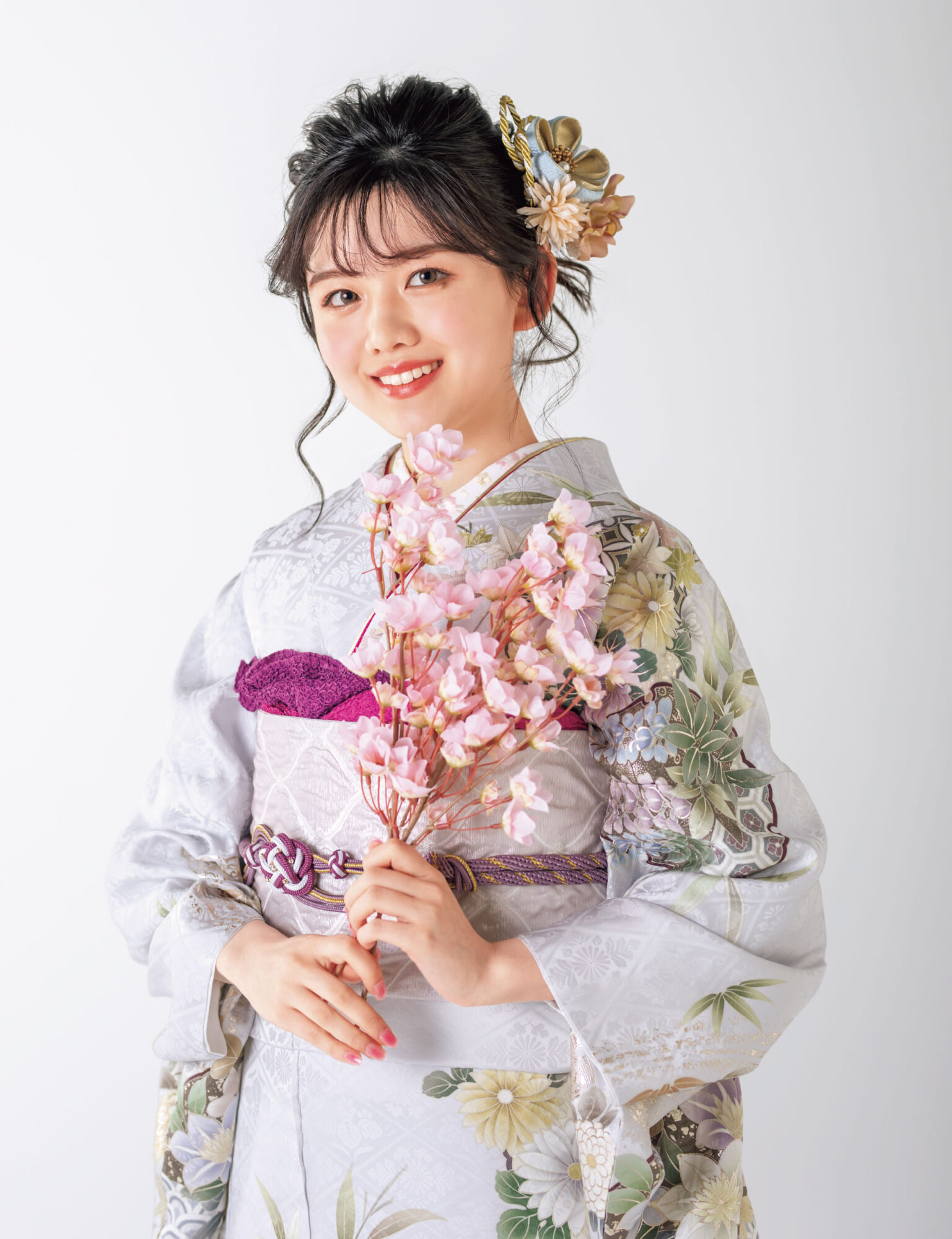 銀鼠色の振袖に白と紫の花々をあしらい、紫の帯締を合わせた女性の立ち姿