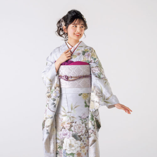 銀鼠色の振袖に白と紫の花々をあしらい、紫の帯締を合わせた女性の立ち姿