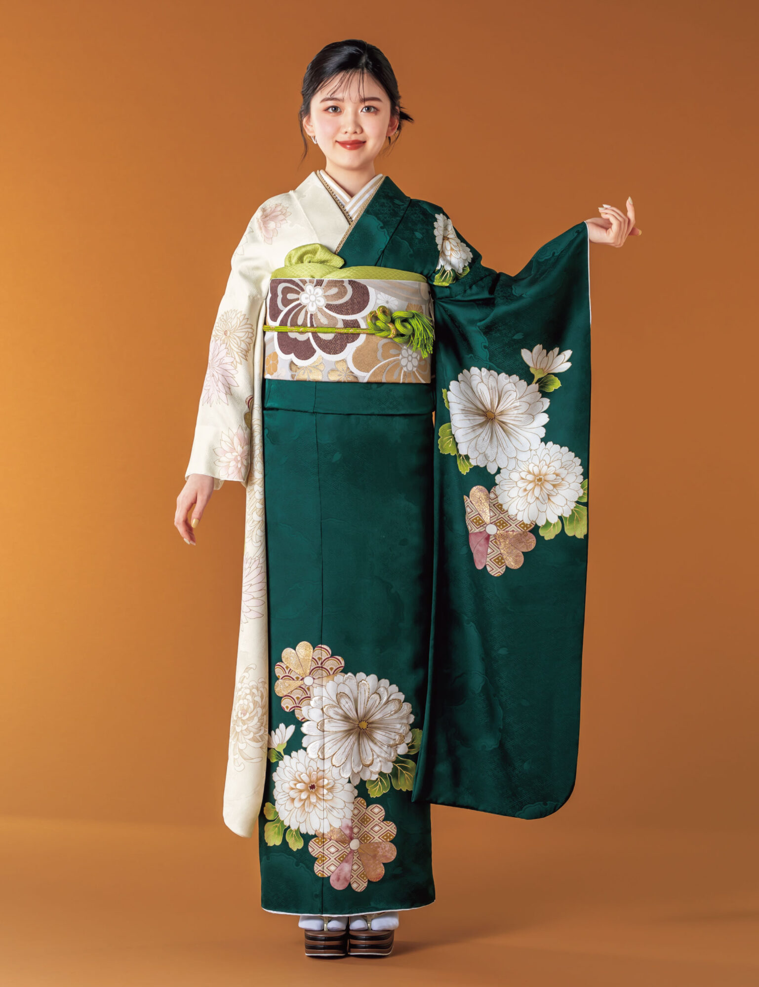 深緑と白の振袖に菊とダリアをあしらい、淡彩の帯と帯締を合わせた女性の立ち姿