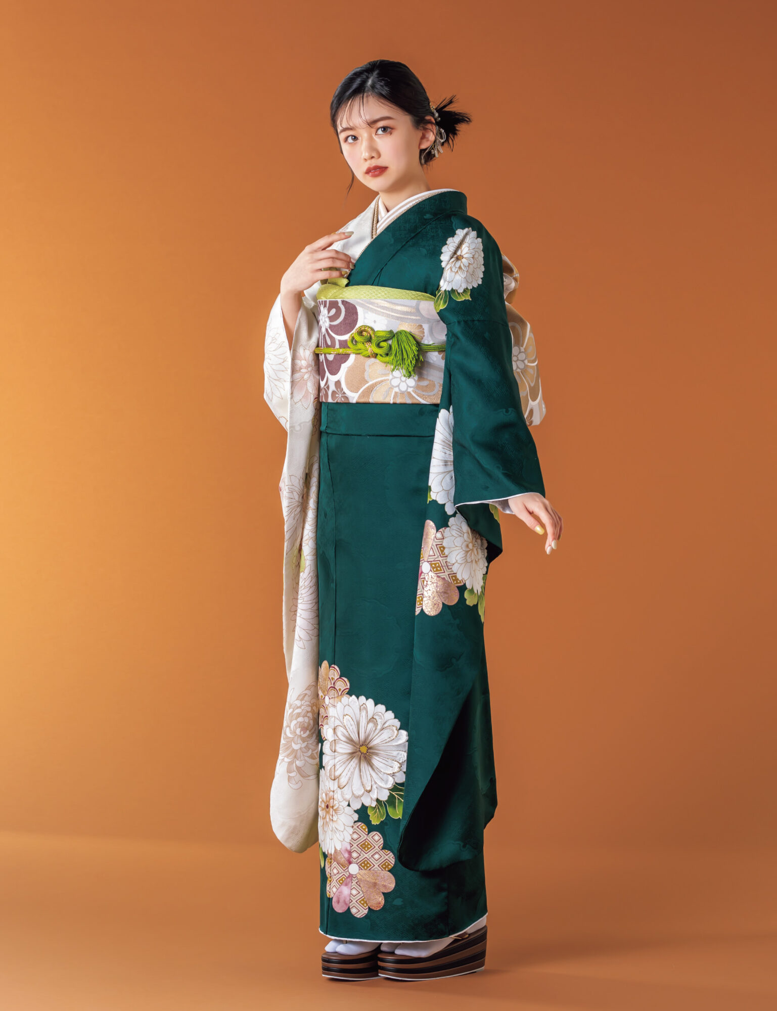 深緑と白の振袖に菊とダリアをあしらい、淡彩の帯と帯締を合わせた女性の立ち姿