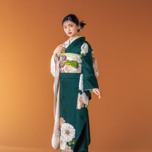 深緑と白の振袖に菊とダリアをあしらい、淡彩の帯と帯締を合わせた女性の立ち姿