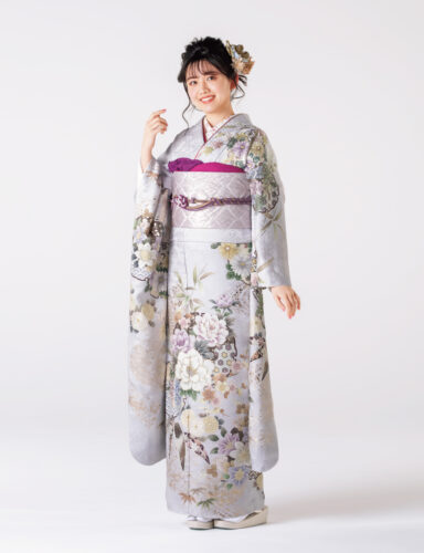 銀鼠色の振袖に白と紫の花々をあしらい、紫の帯締を合わせた女性の立ち姿
