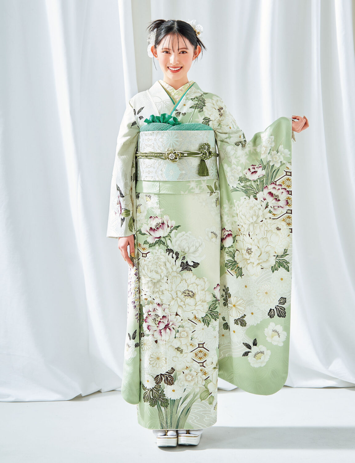 若草色に芍薬が描かれた振袖を着た女性。銀の帯に緑の帯締を合わせ、春らしい気品ある装い。