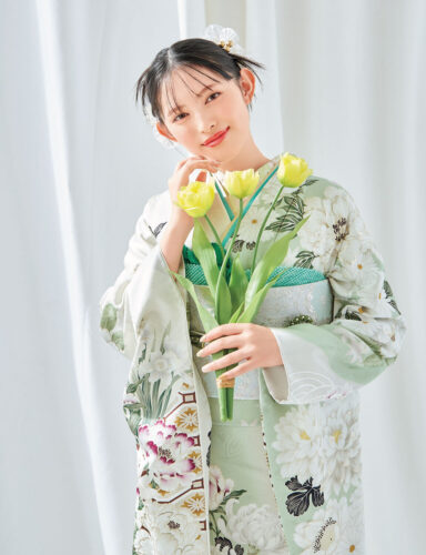 若草色に芍薬が描かれた振袖を着た女性。銀の帯に緑の帯締を合わせ、春らしい気品ある装い。