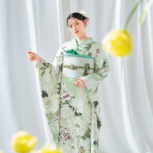 若草色に芍薬が描かれた振袖を着た女性。銀の帯に緑の帯締を合わせ、春らしい気品ある装い。