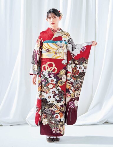 菊と梅の文様が施された白黒金の振袖を着た女性。青の帯締と花の髪飾りが印象的。