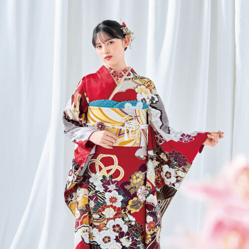 菊と梅の文様が施された白黒金の振袖を着た女性。青の帯締と花の髪飾りが印象的。