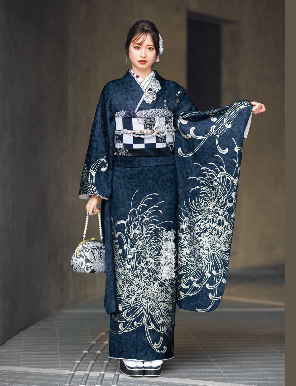 藍地に銀の菊模様が施された振袖姿の女性。帯締とバッグが調和し、優美な印象を与える装い。