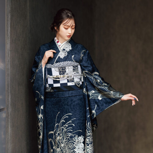 藍地に銀の菊模様が施された振袖姿の女性。帯締とバッグが調和し、優美な印象を与える装い。