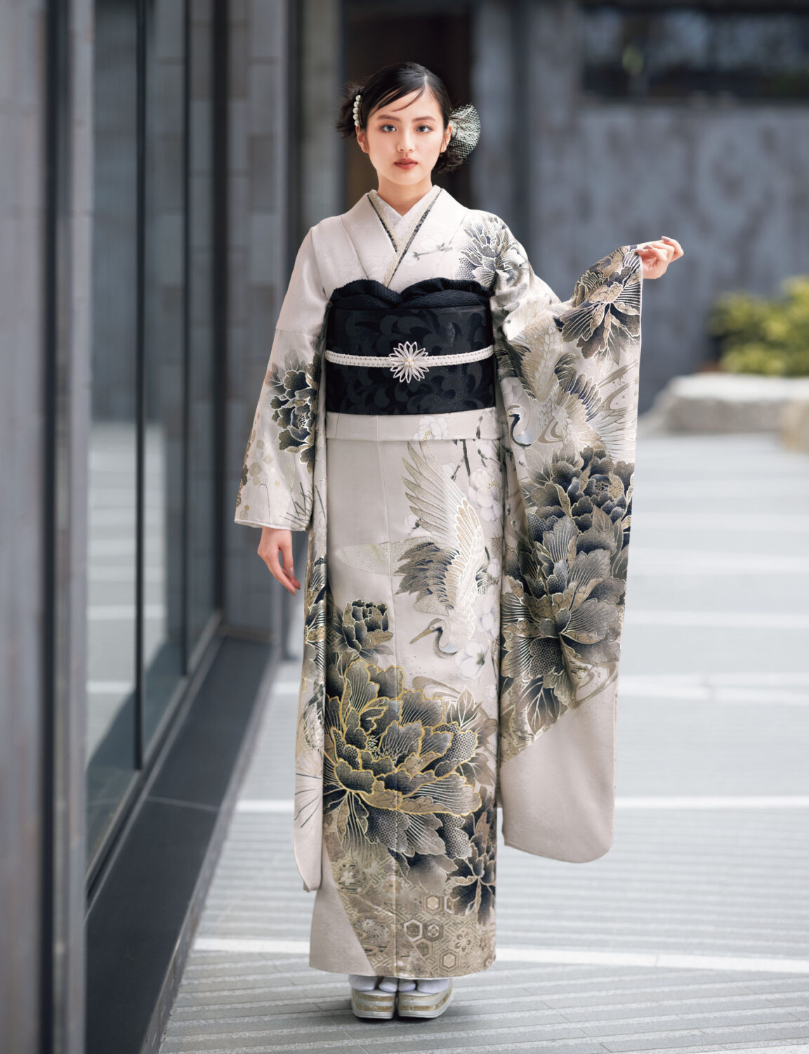 鶴と花模様の振袖を着た女性が、黒の帯締を合わせて優雅に袖を広げている姿