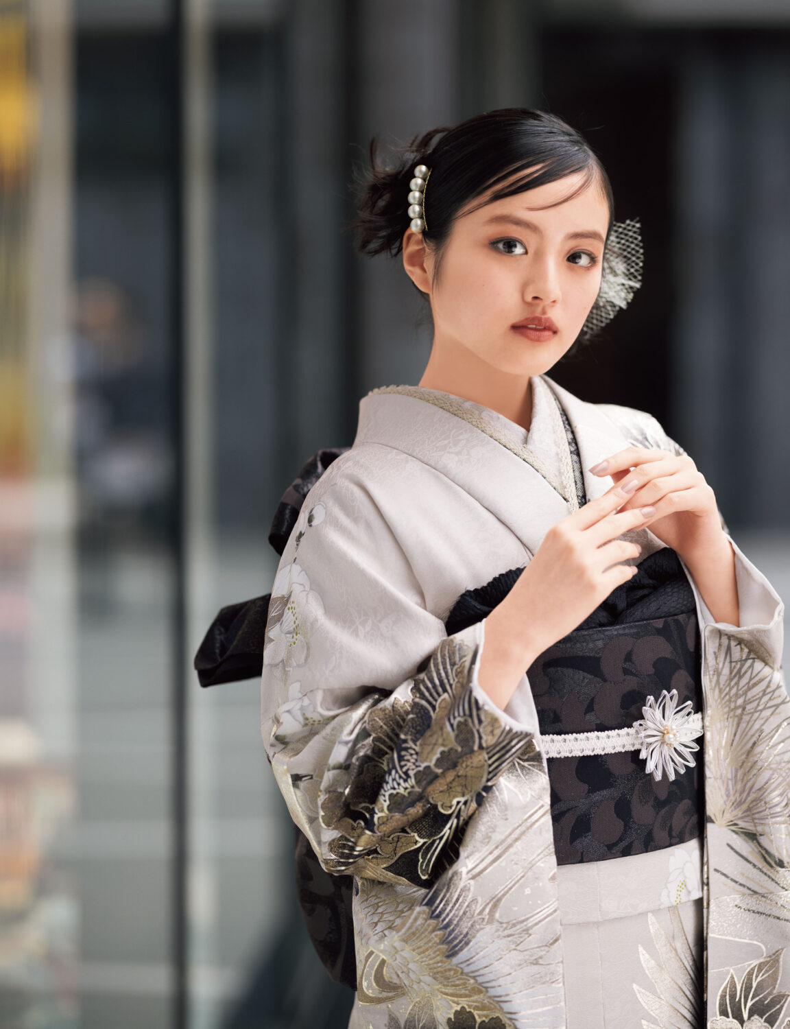 鶴と花模様の振袖を着た女性が、黒の帯締を合わせて優雅に袖を広げている姿