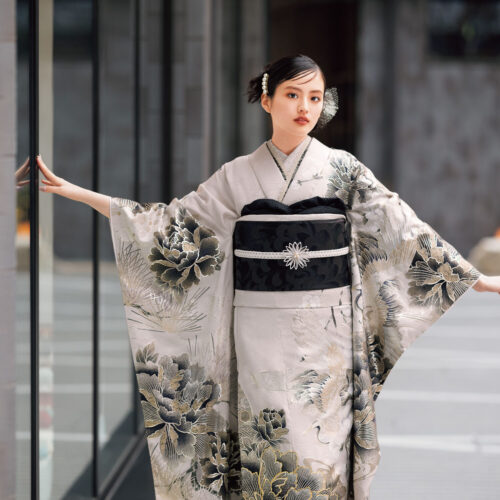 鶴と花模様の振袖を着た女性が、黒の帯締を合わせて優雅に袖を広げている姿