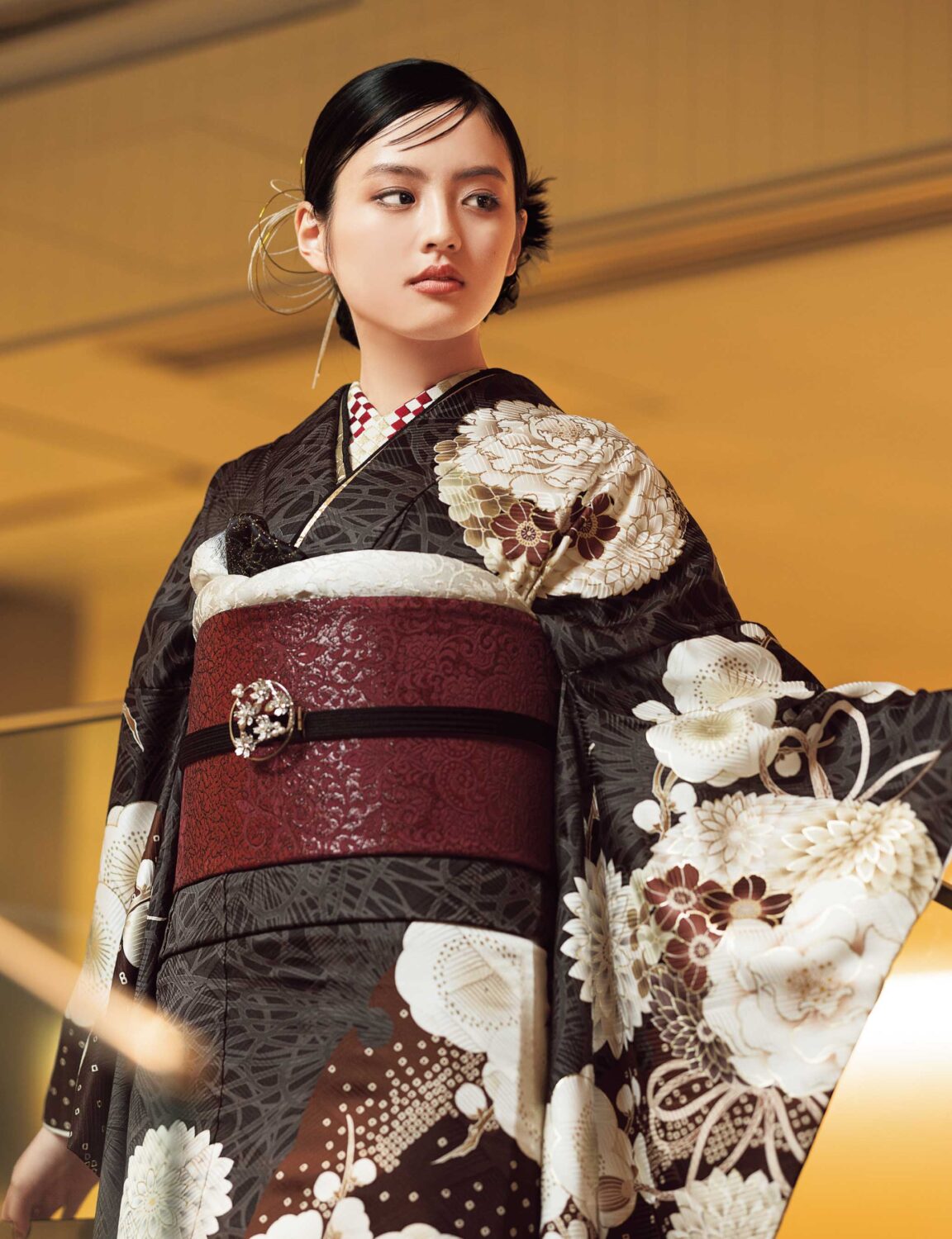 茶系に白花が咲く振袖姿の女性、深紅の帯締と花飾りが上品な印象を演出