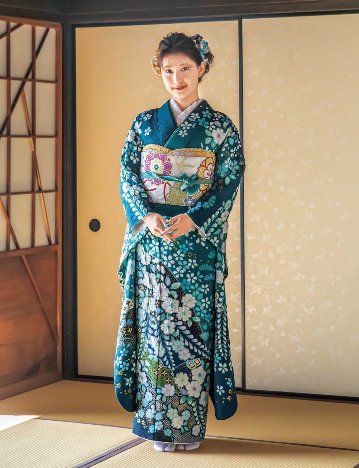 青緑の振袖に白花模様と帯締が映える、格式と華やぎを纏った女性の晴れ姿