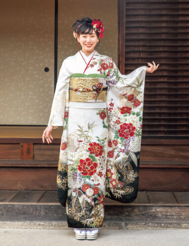 赤白の花柄振袖を着た女性が金の帯締を結び、格式ある装いで立つ姿