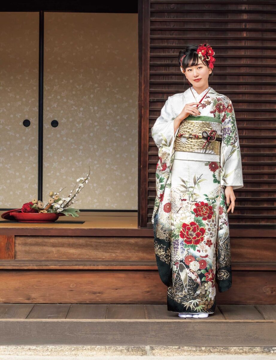 赤白の花柄振袖を着た女性が金の帯締を結び、格式ある装いで立つ姿