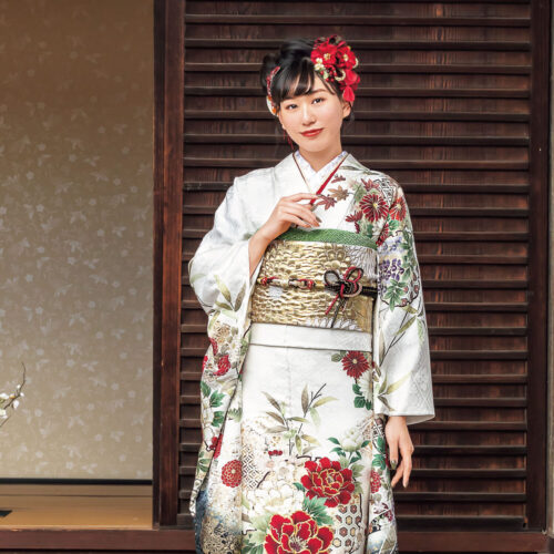 赤白の花柄振袖を着た女性が金の帯締を結び、格式ある装いで立つ姿