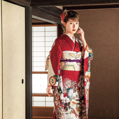 赤地に金彩と花柄が映える振袖姿。帯締と髪飾りが華やかさを添える。