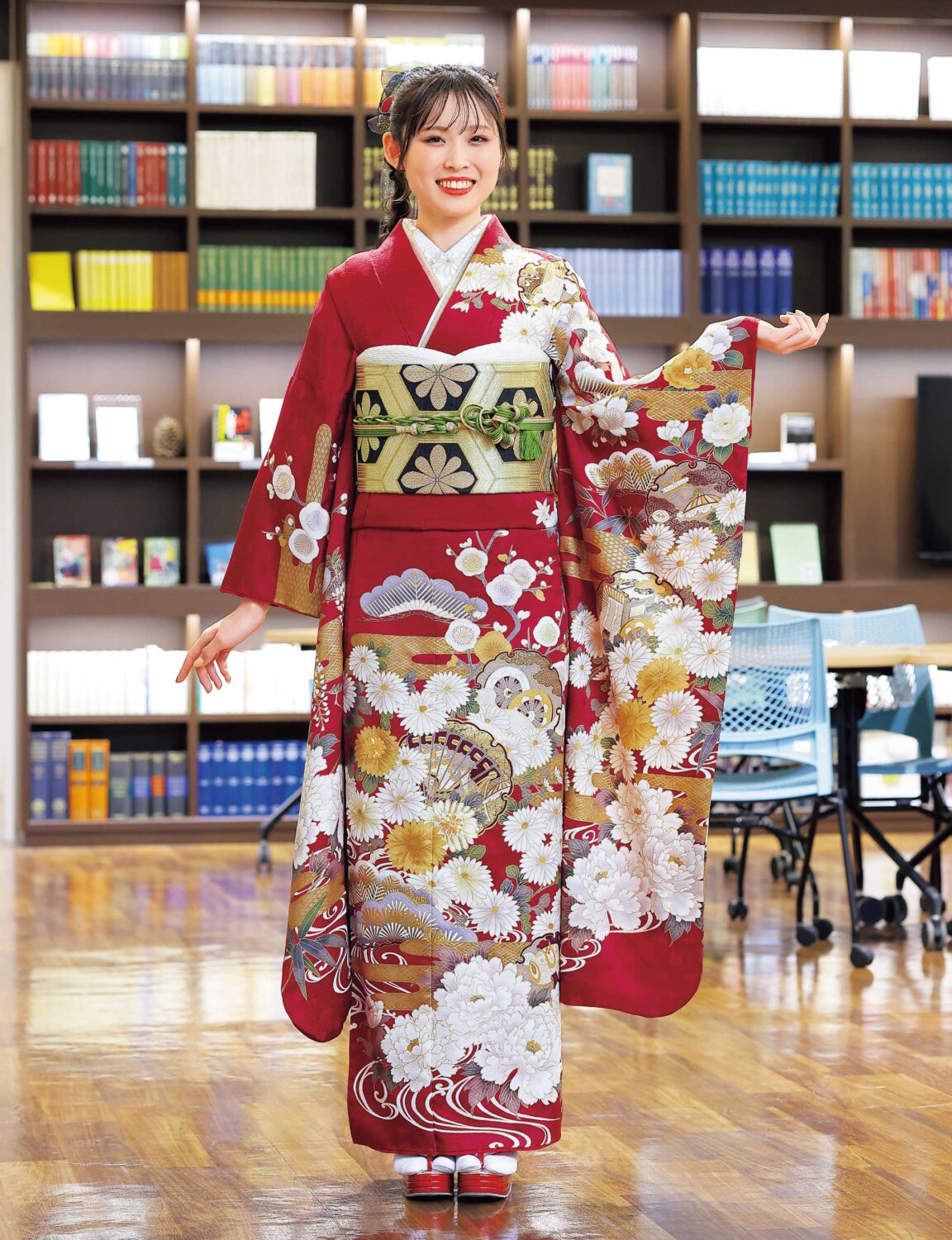 深紅の振袖に菊と金彩があしらわれ、緑の帯締が映える女性の晴れ姿