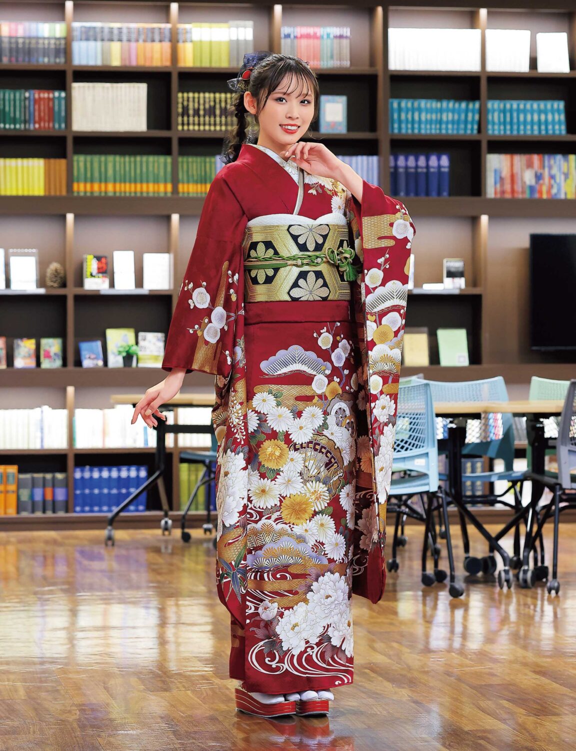 深紅の振袖に菊と金彩があしらわれ、緑の帯締が映える女性の晴れ姿