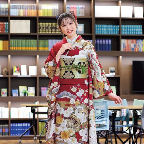 深紅の振袖に菊と金彩があしらわれ、緑の帯締が映える女性の晴れ姿