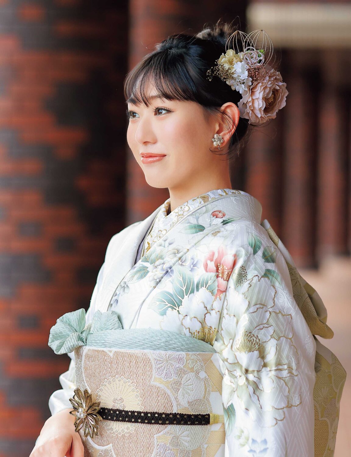 白地に赤・緑・金の菊模様が施された振袖姿の女性。帯締がアクセントになった華やかな装い。