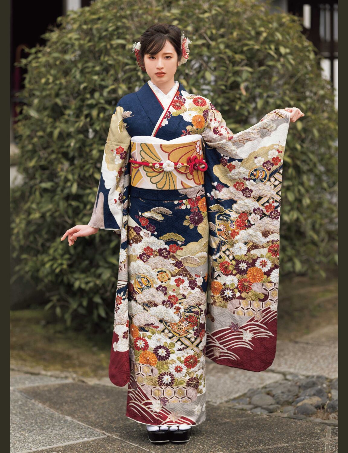 濃紺地に牡丹と菊の花柄が描かれた振袖姿の女性。金の帯締がアクセントになった華やかな装い。