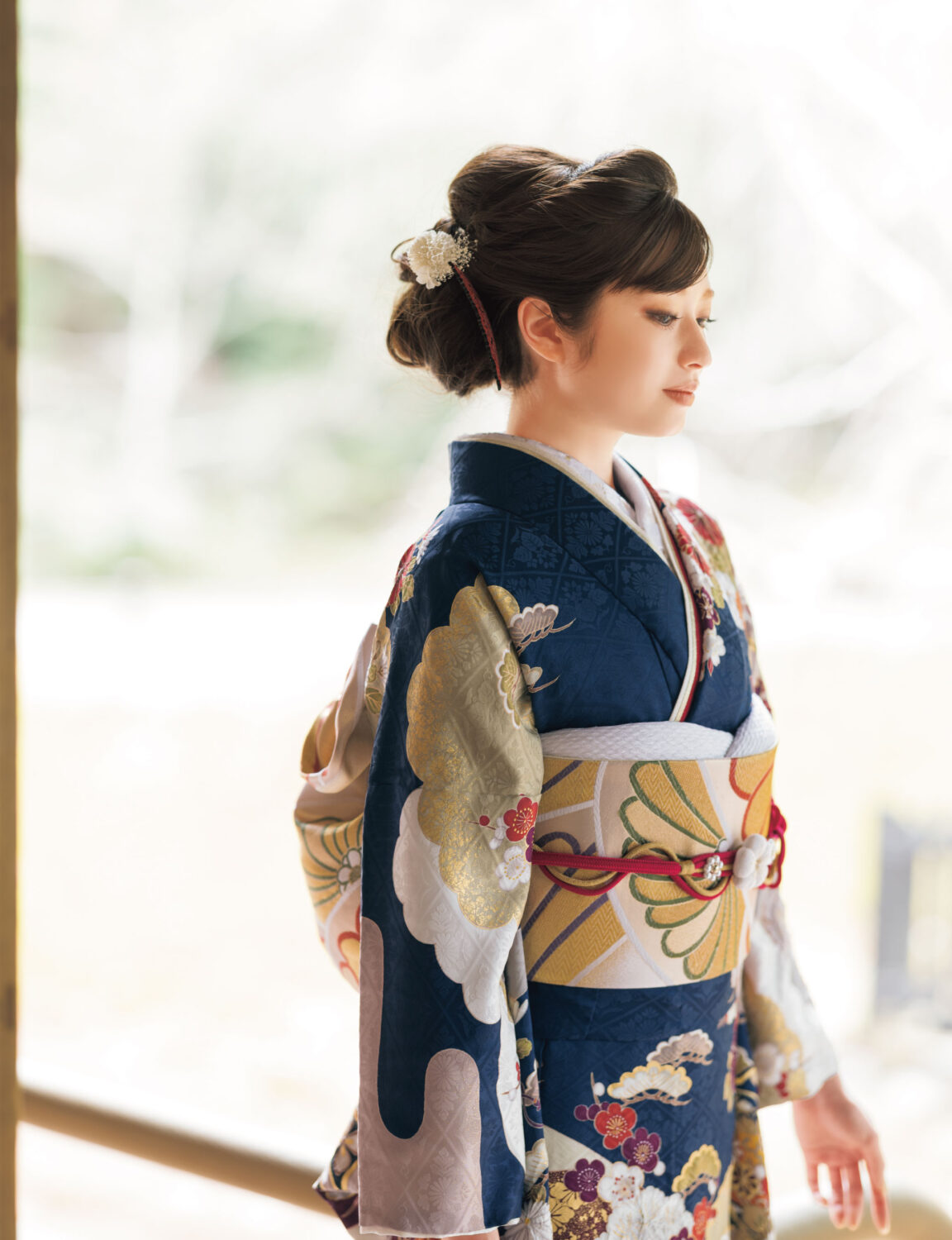 濃紺地に牡丹と菊の花柄が描かれた振袖姿の女性。金の帯締がアクセントになった華やかな装い。