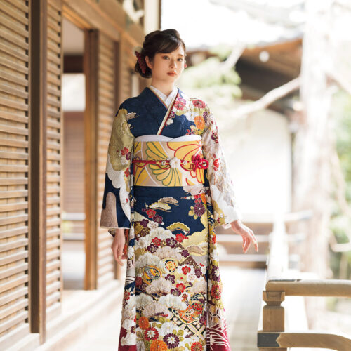 濃紺地に牡丹と菊の花柄が描かれた振袖姿の女性。金の帯締がアクセントになった華やかな装い。