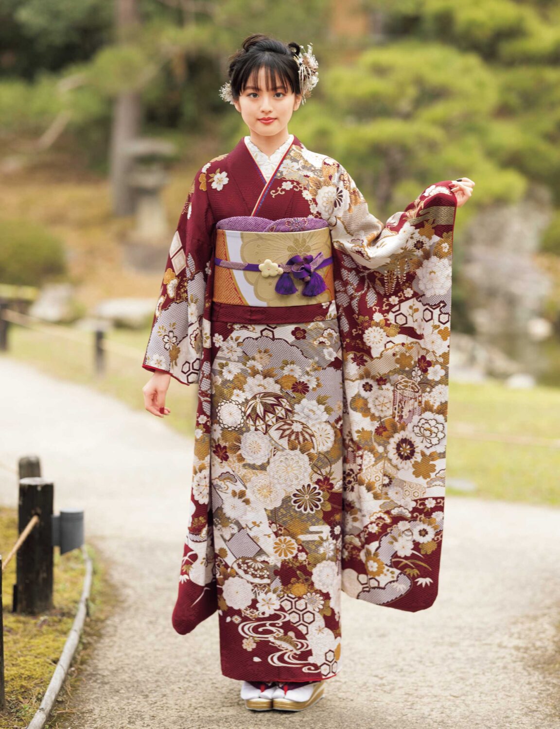 バーガンディに金彩と花柄が施された振袖姿の女性。紫の帯締がアクセント。