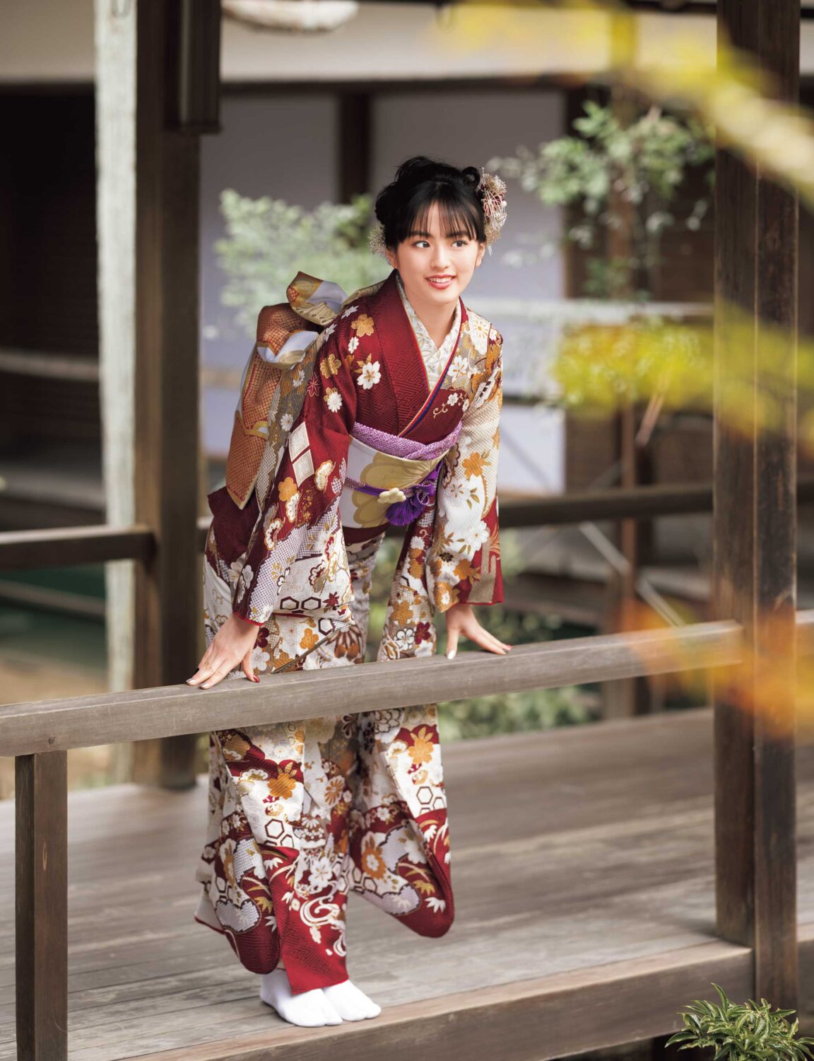 バーガンディに金彩と花柄が施された振袖姿の女性。紫の帯締がアクセント。