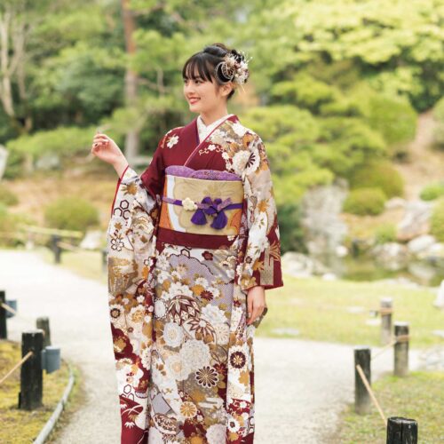 バーガンディに金彩と花柄が施された振袖姿の女性。紫の帯締がアクセント。