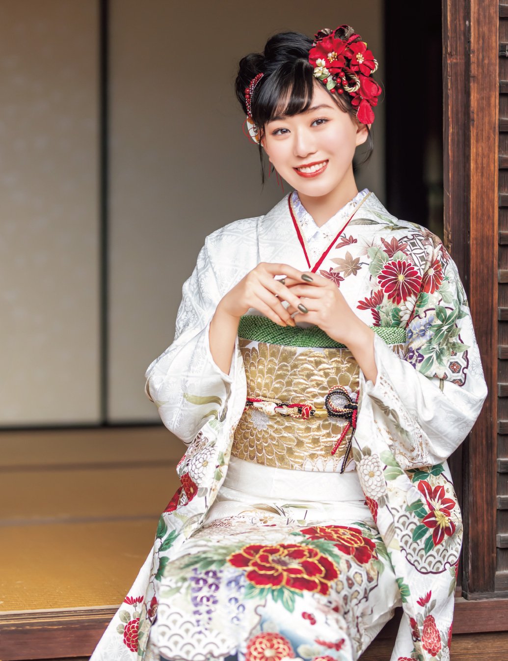 赤白の花柄振袖を着た女性が金の帯締を結び、格式ある装いで立つ姿