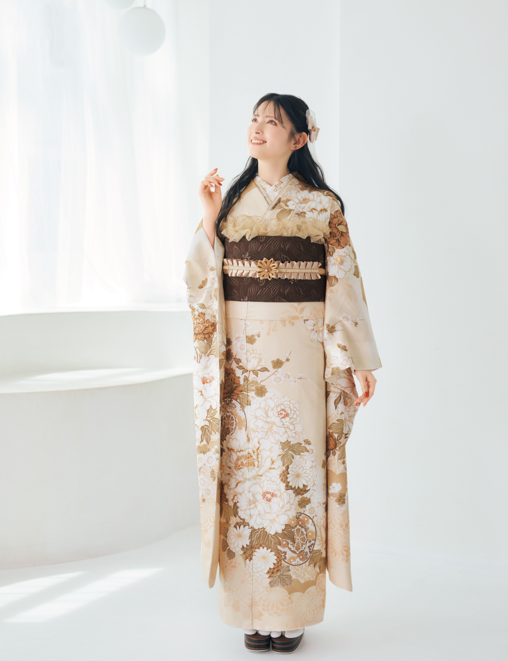 淡いクリーム色に金彩の古典柄が施された振袖を着た女性が、袖を広げて上品なコーディネートを見せている様子。