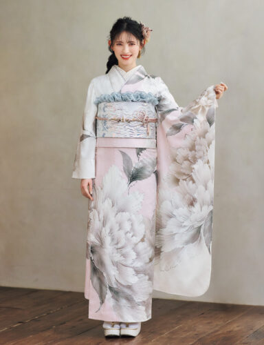 淡いピンクと白の振袖に銀色の花柄をあしらい、青みグレーの帯と帯締を合わせた女性が、上品な晴れ姿を見せている様子。