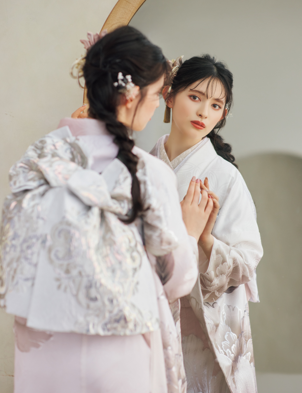 淡いピンクと白の振袖に銀色の花柄をあしらい、青みグレーの帯と帯締を合わせた女性が、上品な晴れ姿を見せている様子。