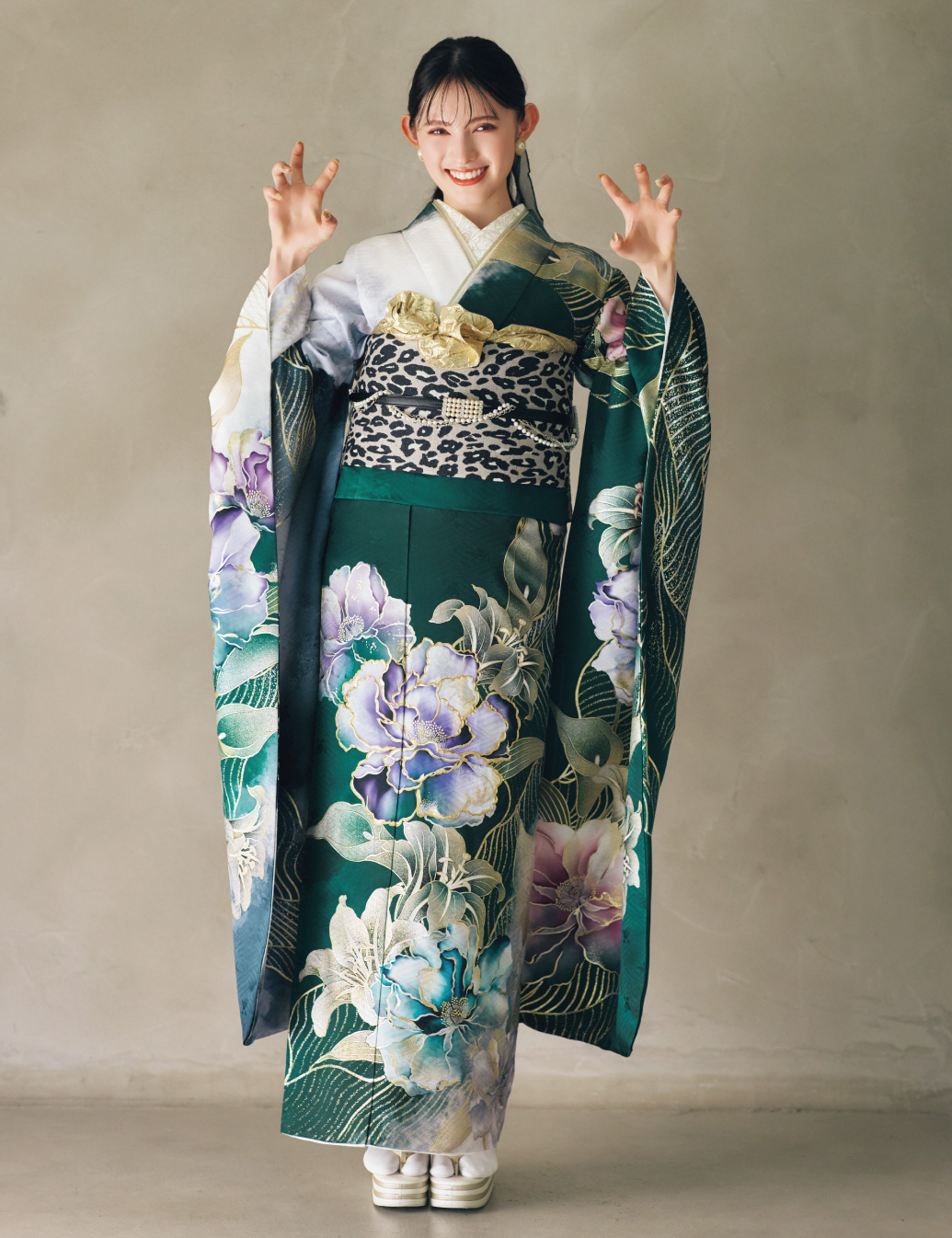 深緑の振袖に大柄の花文様をあしらい、レオパード柄の帯と金の帯締を合わせた女性が、華やかで個性的なコーディネートを見せている様子。