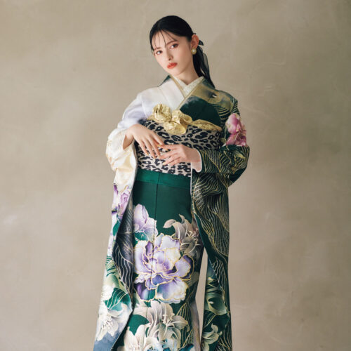 深緑の振袖に大柄の花文様をあしらい、レオパード柄の帯と金の帯締を合わせた女性が、華やかで個性的なコーディネートを見せている様子。