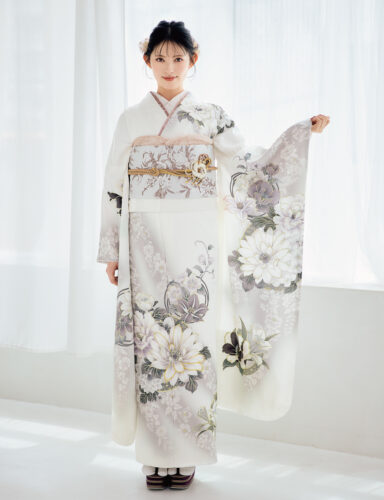 白地に灰色と淡紫の花柄をあしらい、淡色の帯と金の帯締を合わせた女性が、上品な振袖姿を見せている様子。