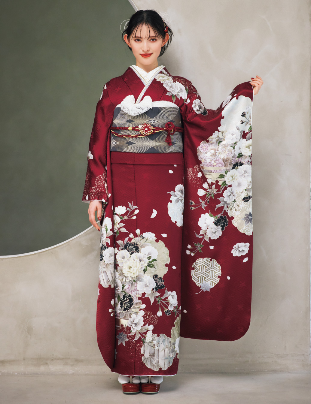 深紅の振袖に白と薄灰の花柄をあしらい、灰色の帯と花の帯締を合わせた女性が、上品で華やかな振袖姿を見せている様子。