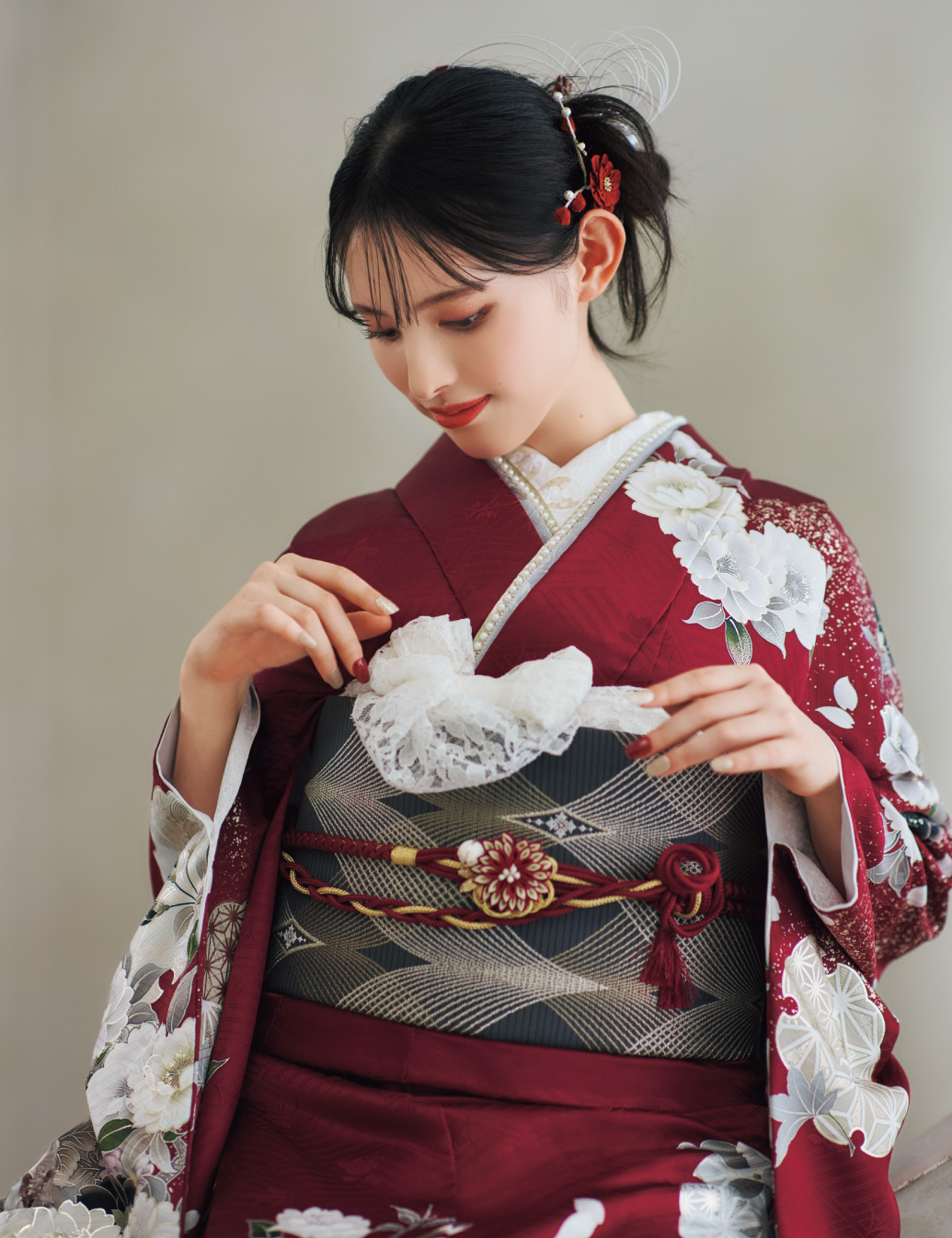 深紅の振袖に白と薄灰の花柄をあしらい、灰色の帯と花の帯締を合わせた女性が、上品で華やかな振袖姿を見せている様子。