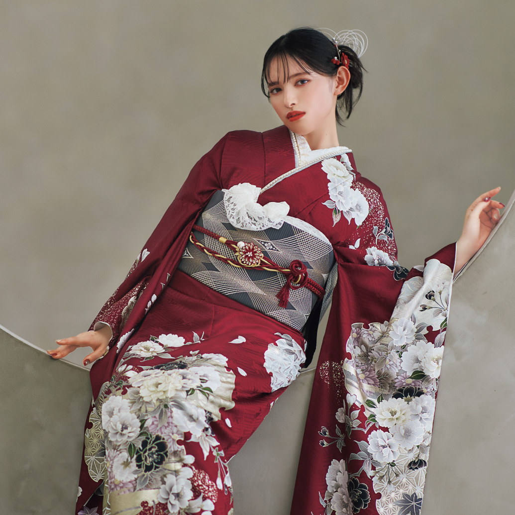 深紅の振袖に白と薄灰の花柄をあしらい、灰色の帯と花の帯締を合わせた女性が、上品で華やかな振袖姿を見せている様子。
