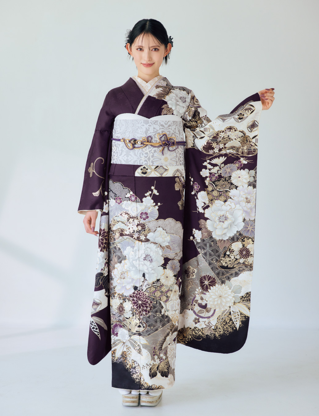 深紫の振袖に金・白・銀の花柄をあしらい、淡色の帯と帯締を合わせた女性が、上品で華やかな振袖姿を見せている様子。