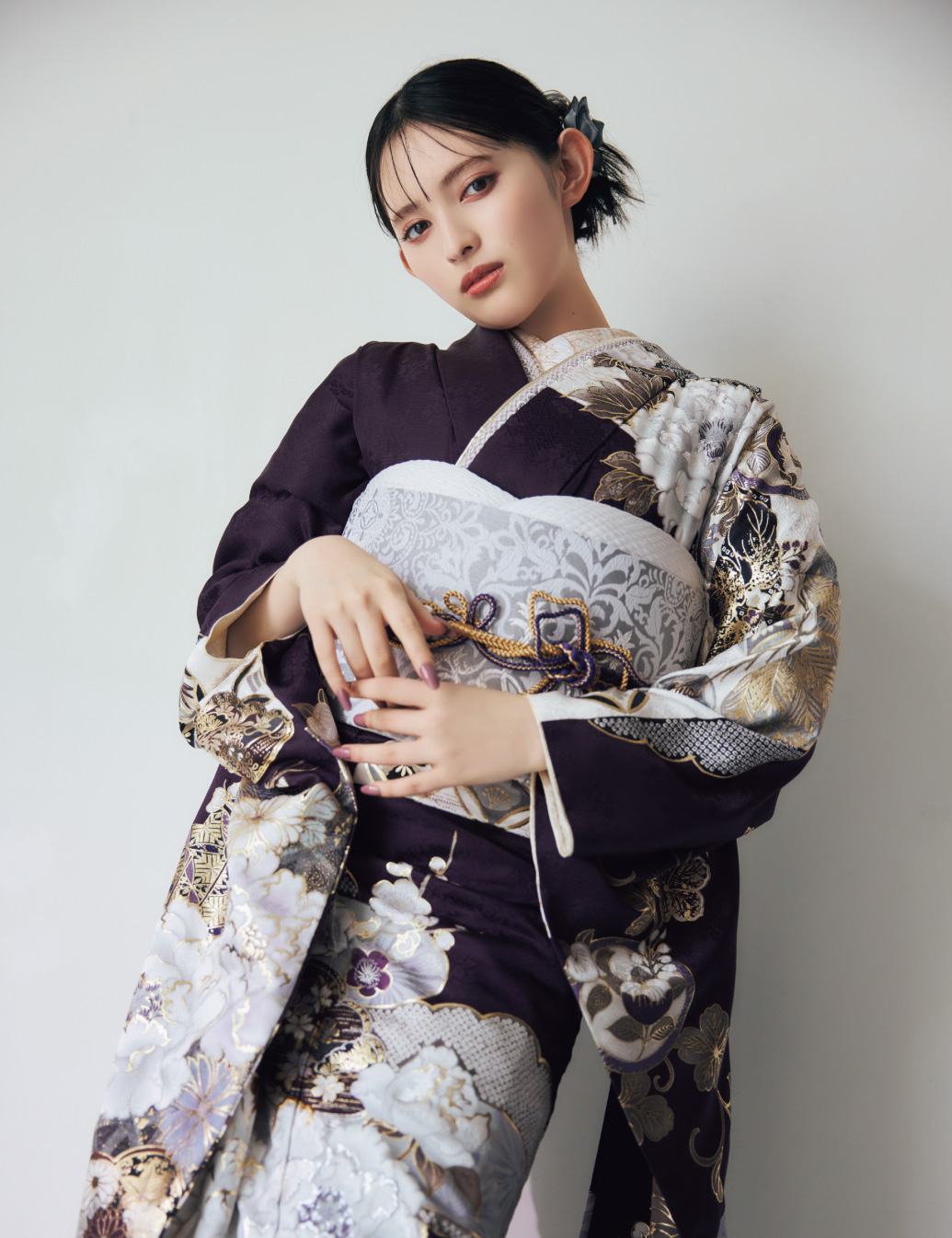 深紫の振袖に金・白・銀の花柄をあしらい、淡色の帯と帯締を合わせた女性が、上品で華やかな振袖姿を見せている様子。