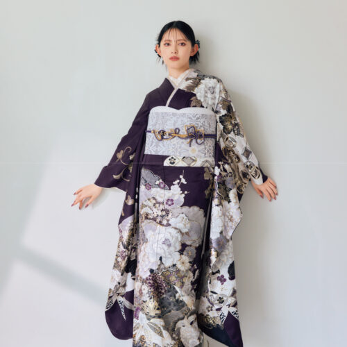 深紫の振袖に金・白・銀の花柄をあしらい、淡色の帯と帯締を合わせた女性が、上品で華やかな振袖姿を見せている様子。