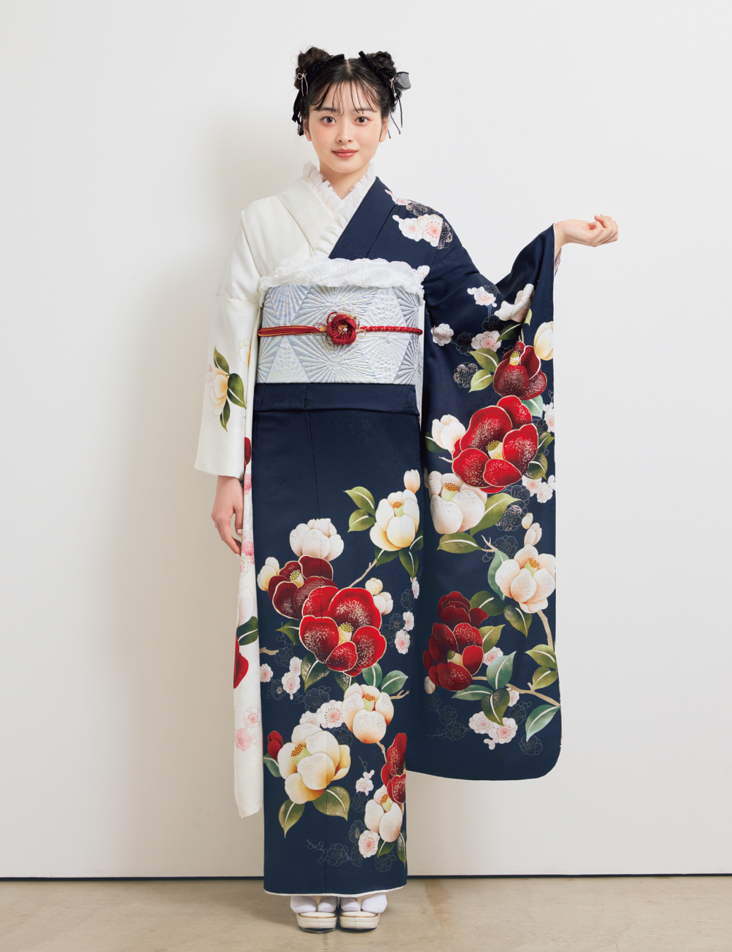白×紺の切り替え振袖に赤・白・桃の花柄をあしらい、淡色の帯と赤の帯締を合わせた女性が、華やかな振袖姿を見せている様子。
